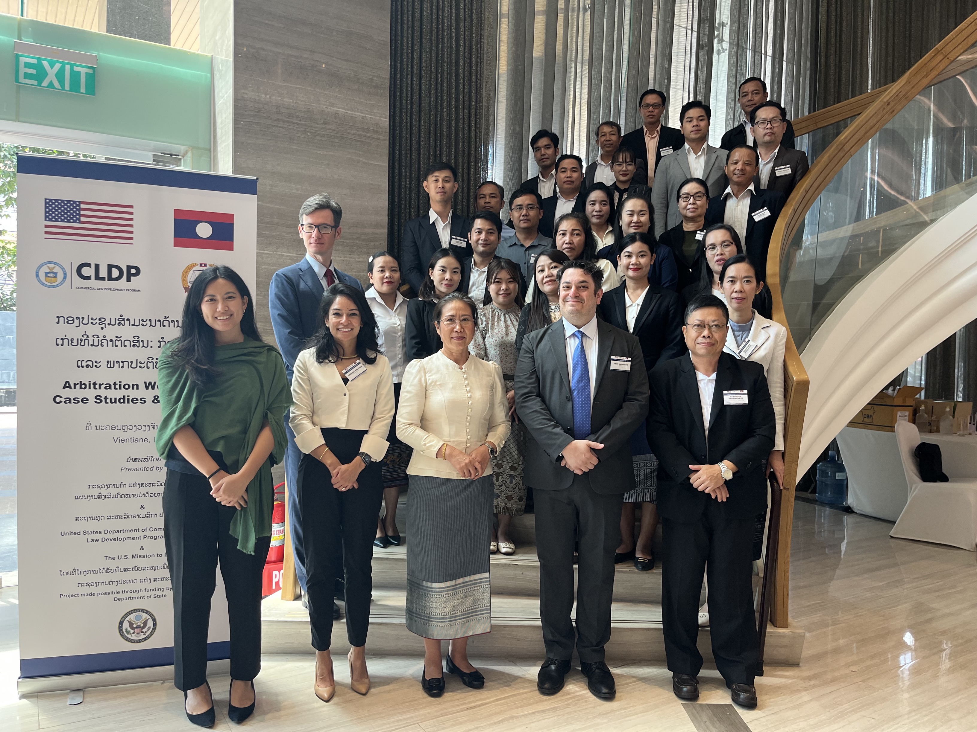 Participant photo with all Lao ADR participants. There is a banner on the left around 6 ft tall with the title: Arbitration Workshop: Case Studies &amp; Practice. There are 35 people standing on a cascading staircase.